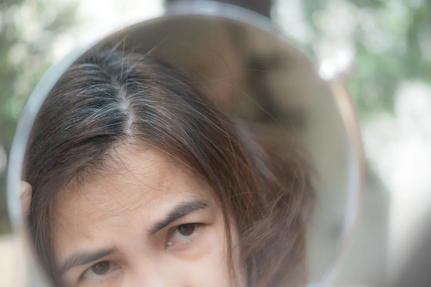 middle aged woman looking at her hair in a mirror