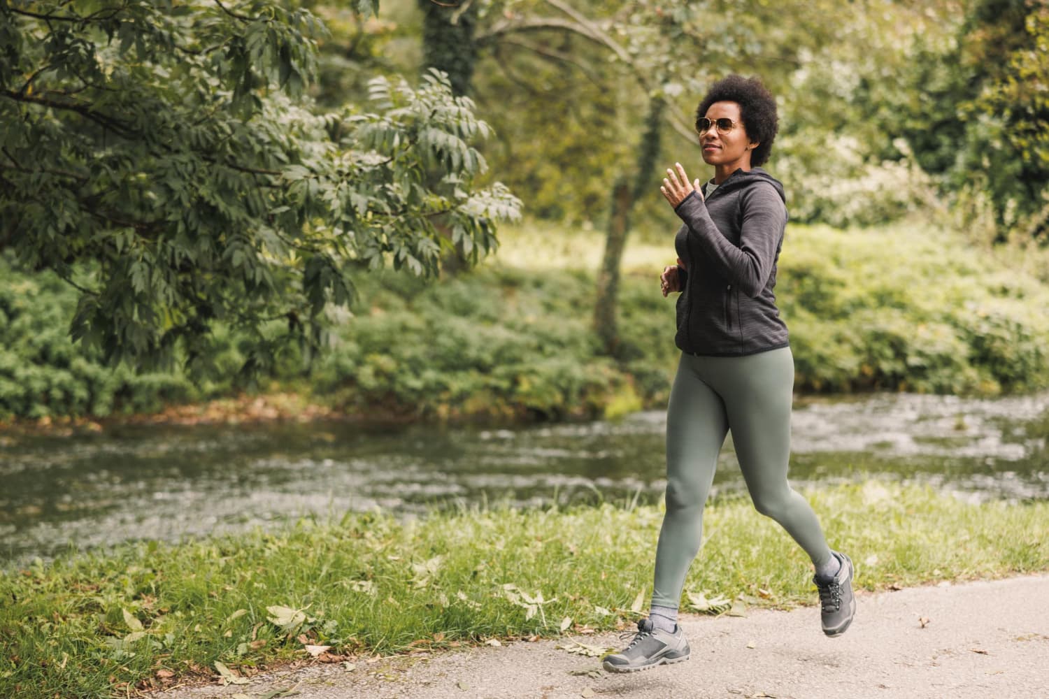 beautiful smiling mature african american woman is running along trail near mountains river nature