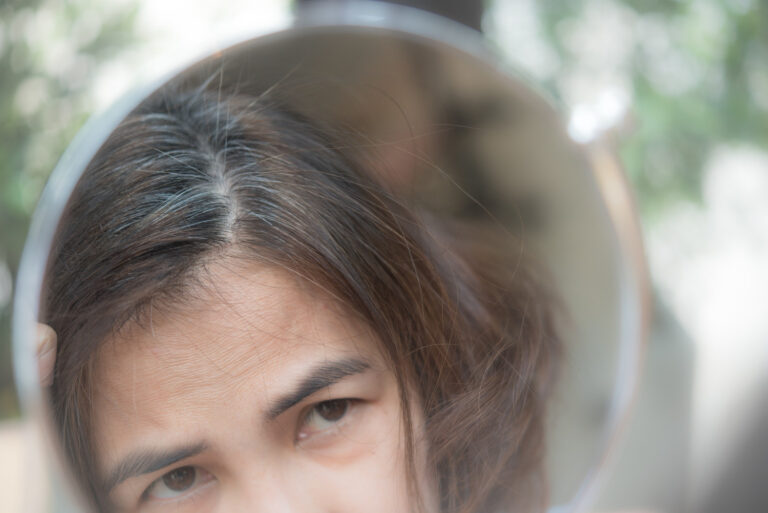 middle aged woman looking at her hair in a mirror